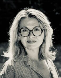 Portrait en noir et blanc d'Annabella Troudi, Hypnothérapeute certifiée, expérimentée et bienveillante. Elle porte des lunettes, en extérieur, souriante et confiante.